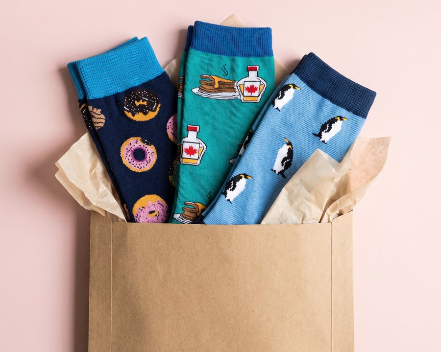 Three pairs of moJJa crew socks with donuts, pancakes and penguins tucked in a kraft envelope